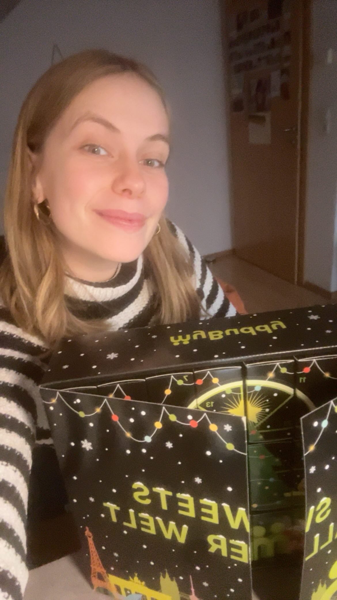 myBuddy Community-Foto: Blonde Frau im Streifenrolli hält den geöffneten SWEETS-Kalender ins Selfie, Flurhintergrund
