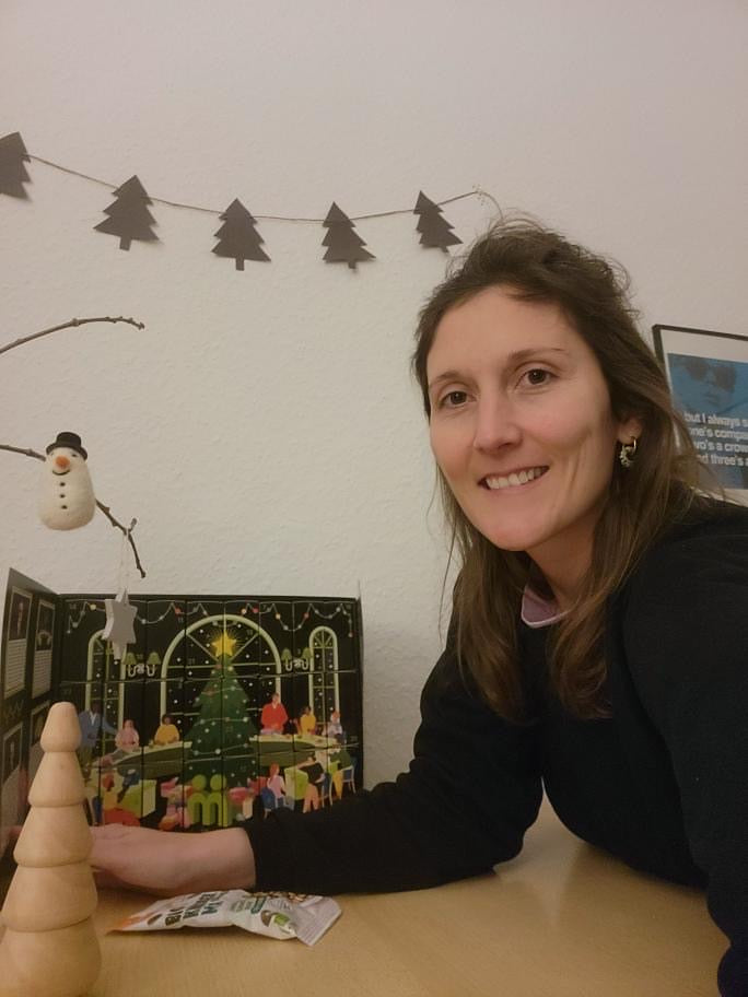 myBuddy Community-Foto: Frau am Tisch neben dem aufgeklappten Kalender, Tannenbaum-Girlande und Filzschneemann an der Wand