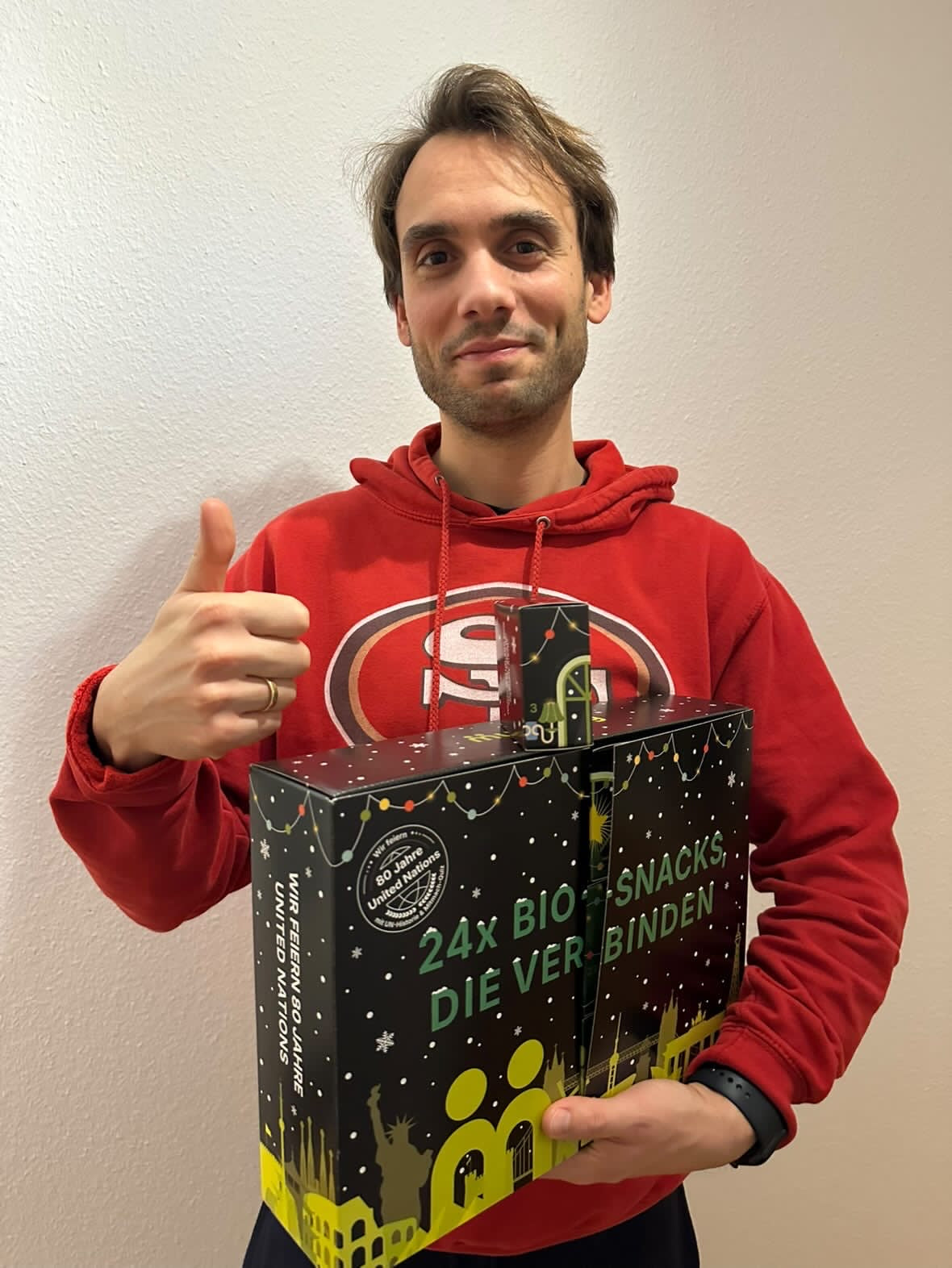 myBuddy Community-Foto: Mann im roten 49ers-Hoodie, Daumen hoch, hält Kalender samt herausgenommenem Türchen-Döschen