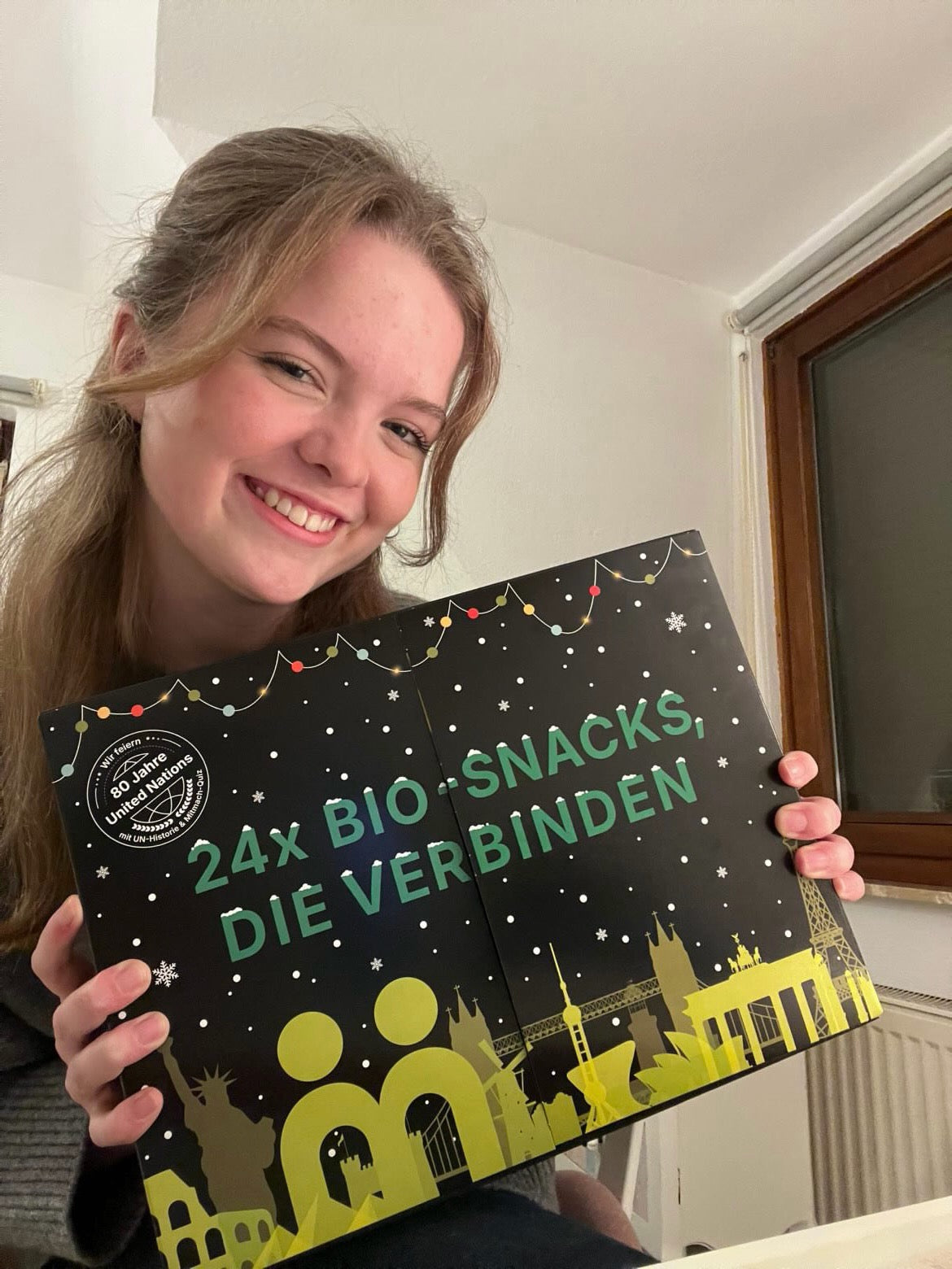myBuddy Community-Foto: Junge Frau am Fenster hält den Kalender lachend vor sich, Heizkörper und Holzfenster im Bild