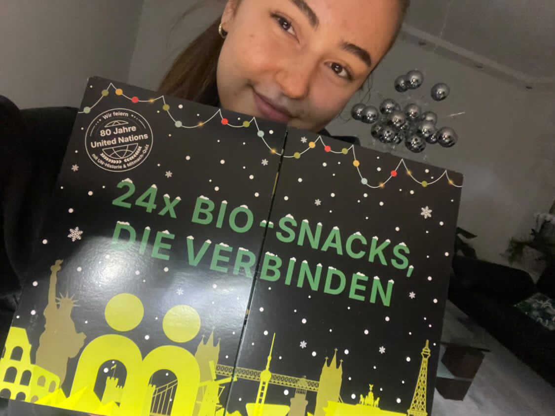 myBuddy Community-Foto: Frau lugt hinter dem hochgehaltenen Kalender hervor, silberne Kugeln als Deko im Hintergrund