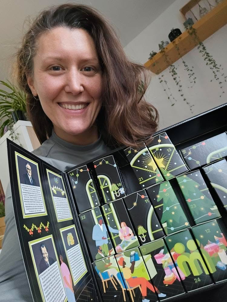 myBuddy Community-Foto: Frau präsentiert den vollständig aufgeklappten Kalender mit UN-Infotafeln, Zimmerpflanzen im Hintergrund