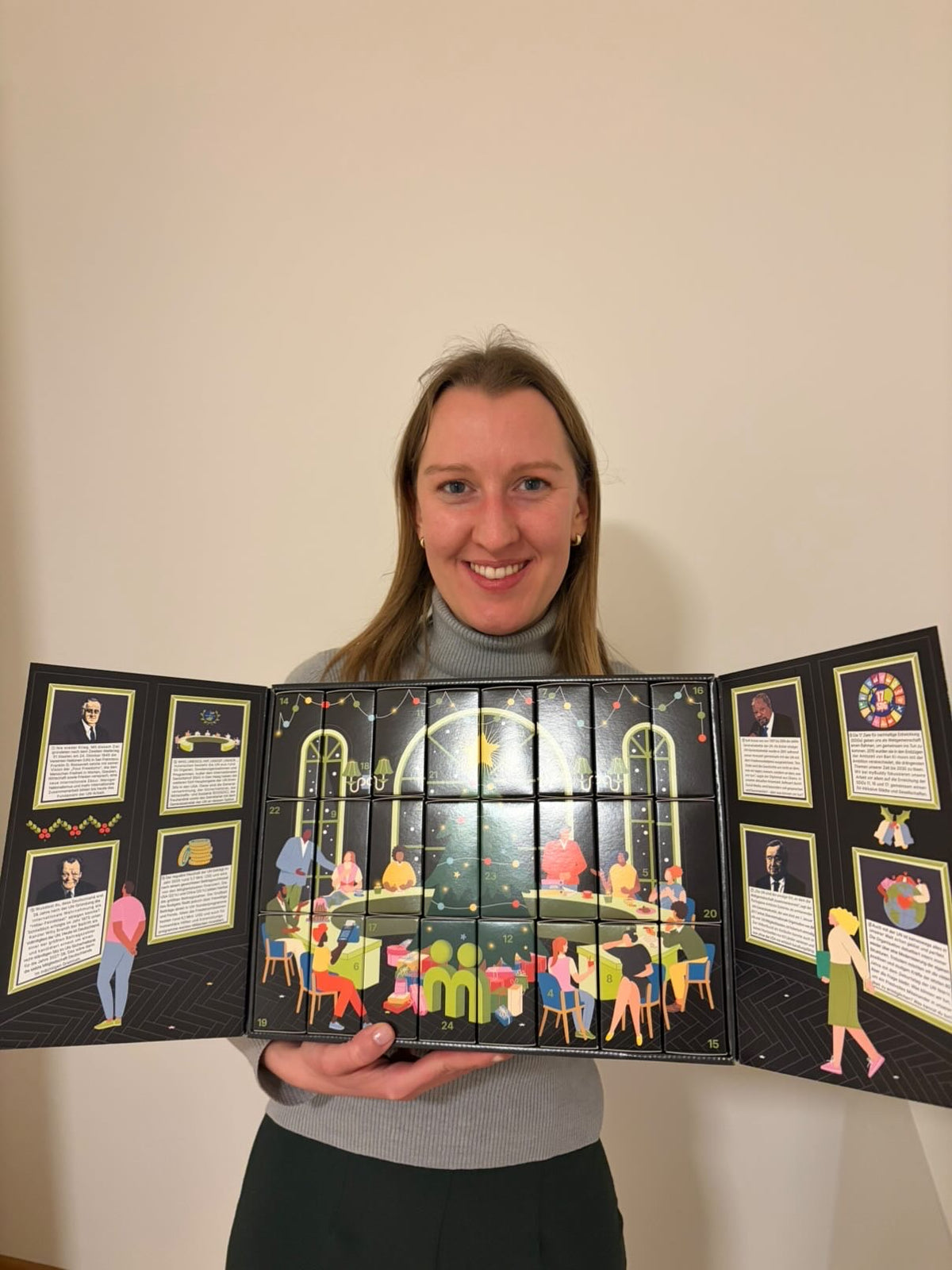 myBuddy Community-Foto: Frau im grauen Rolli hält den komplett aufgeklappten Kalender mit beiden UN-Infoflügeln vor weißer Wand
